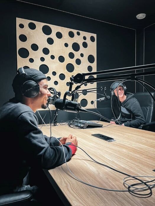 Podcast studio with two smiling hosts around a table equipped with microphones