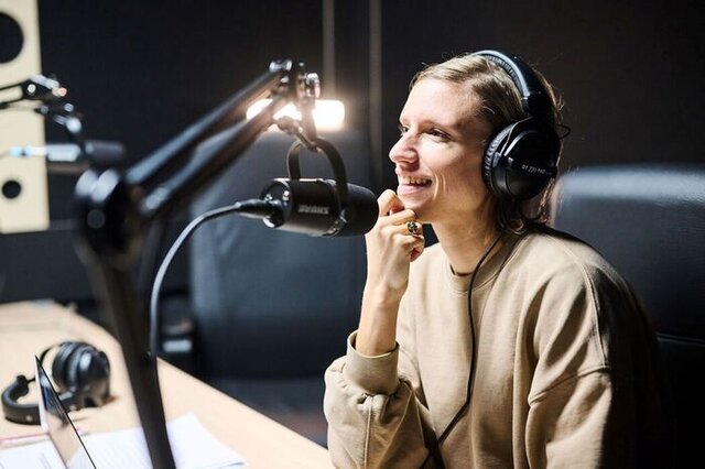 woman recording a podcast, wearing headphones and in front of a podcast microphone in a professional podcast studio