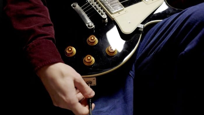 Black guitar with brass buttons and musician plugging jack into guitar