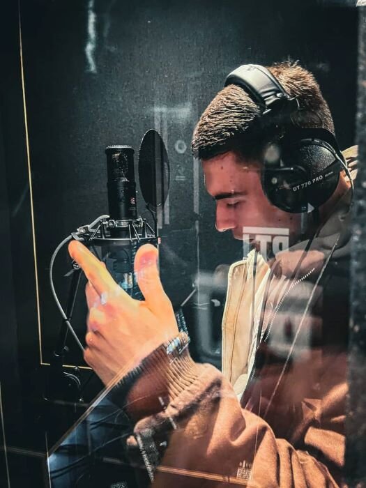 Singer in front of a microphone with headphones on in the vocal booth of a recording studio 