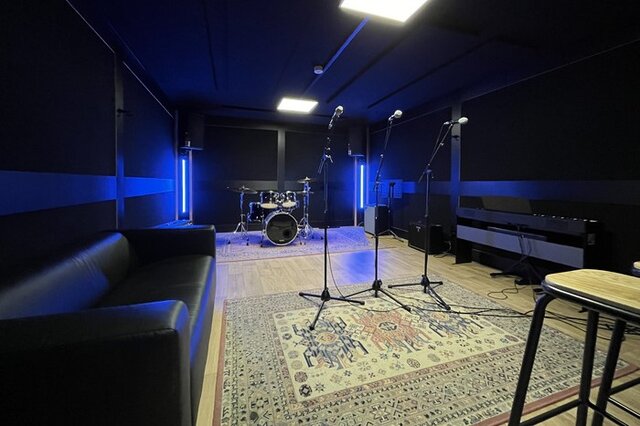 Large rehearsal studio with piano, drums, and blue LED lighting